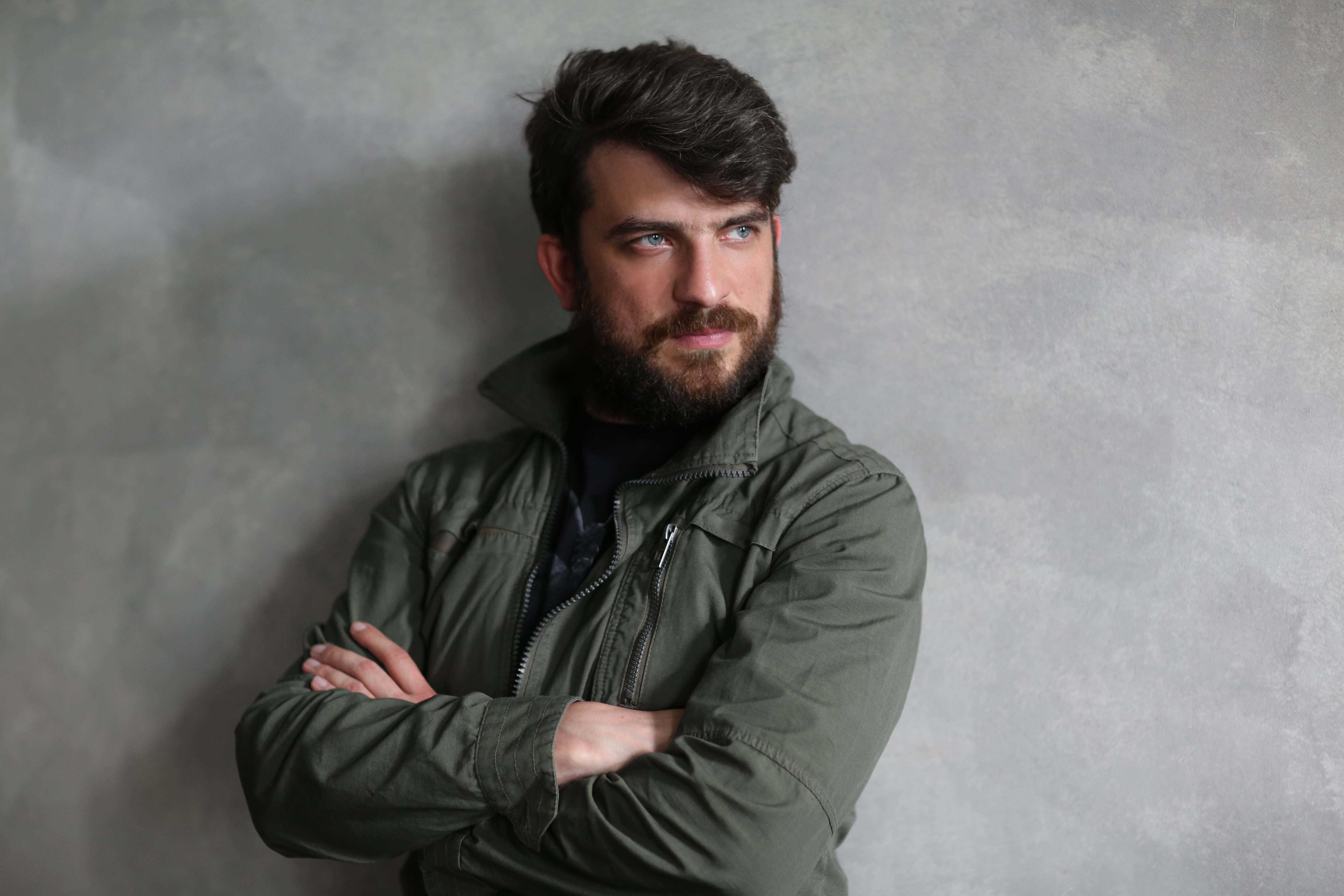 Guy in khaki jacket leaning on wall with crossed hands. Close.up. Black
